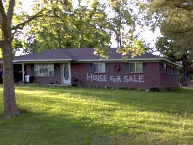 Neglected home with "House for sale" spray painted on the brick exterior.